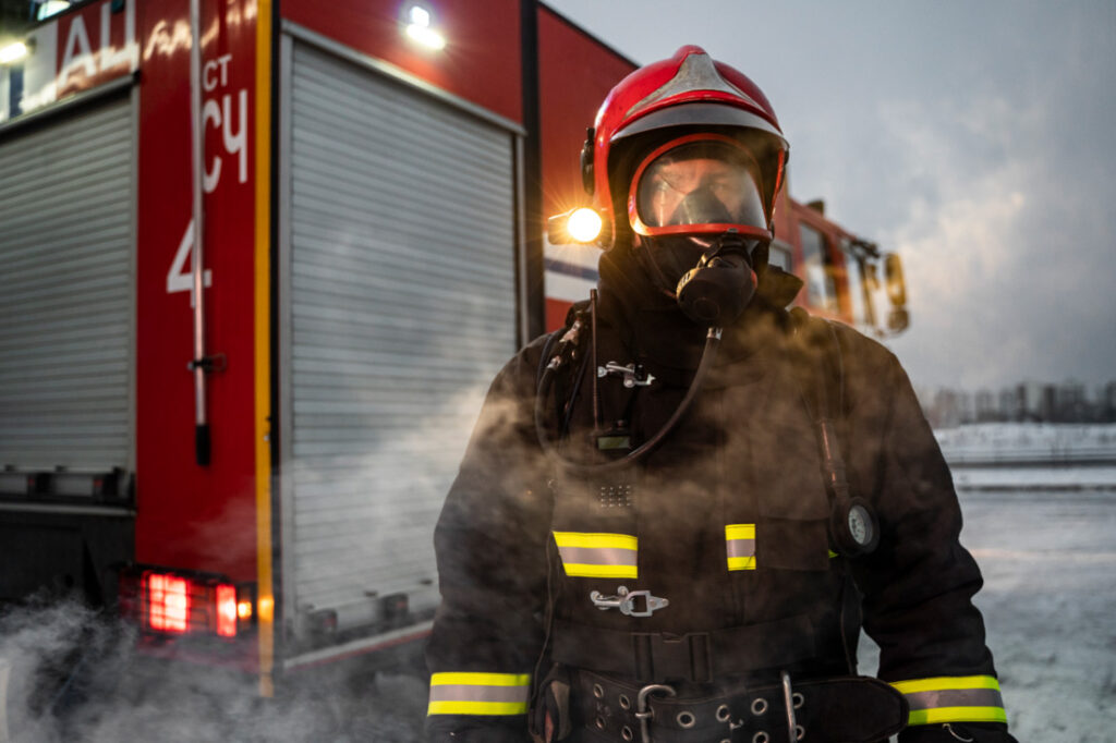 Photo of a firefighter next to a red fire track wearing full gear, oxygen mask and helmet to illustrate how mental health can affect first responders.